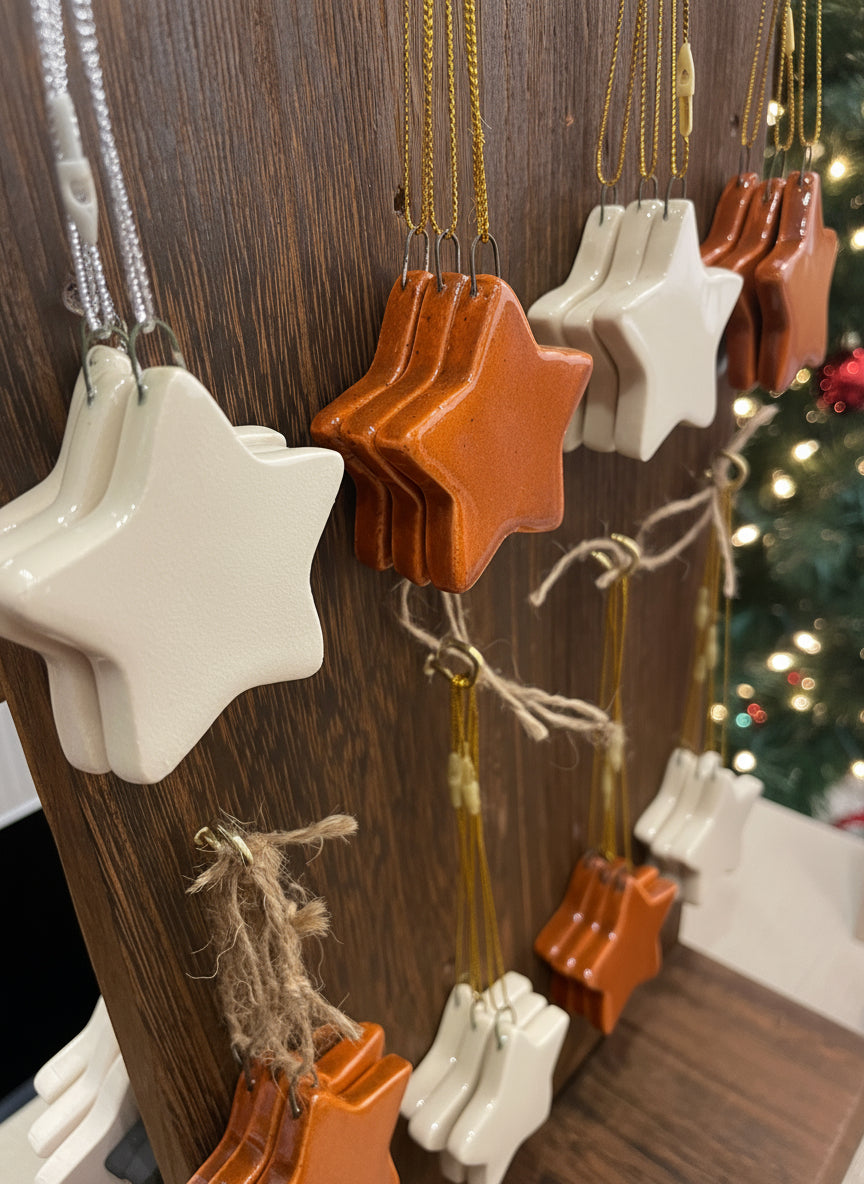 A set of three white star-shaped ceramic ornaments with a high-gloss finish, displayed hanging against a wooden background.